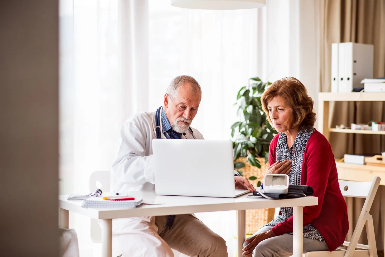 Male doctor with laptop talking to a senior woman in his office.