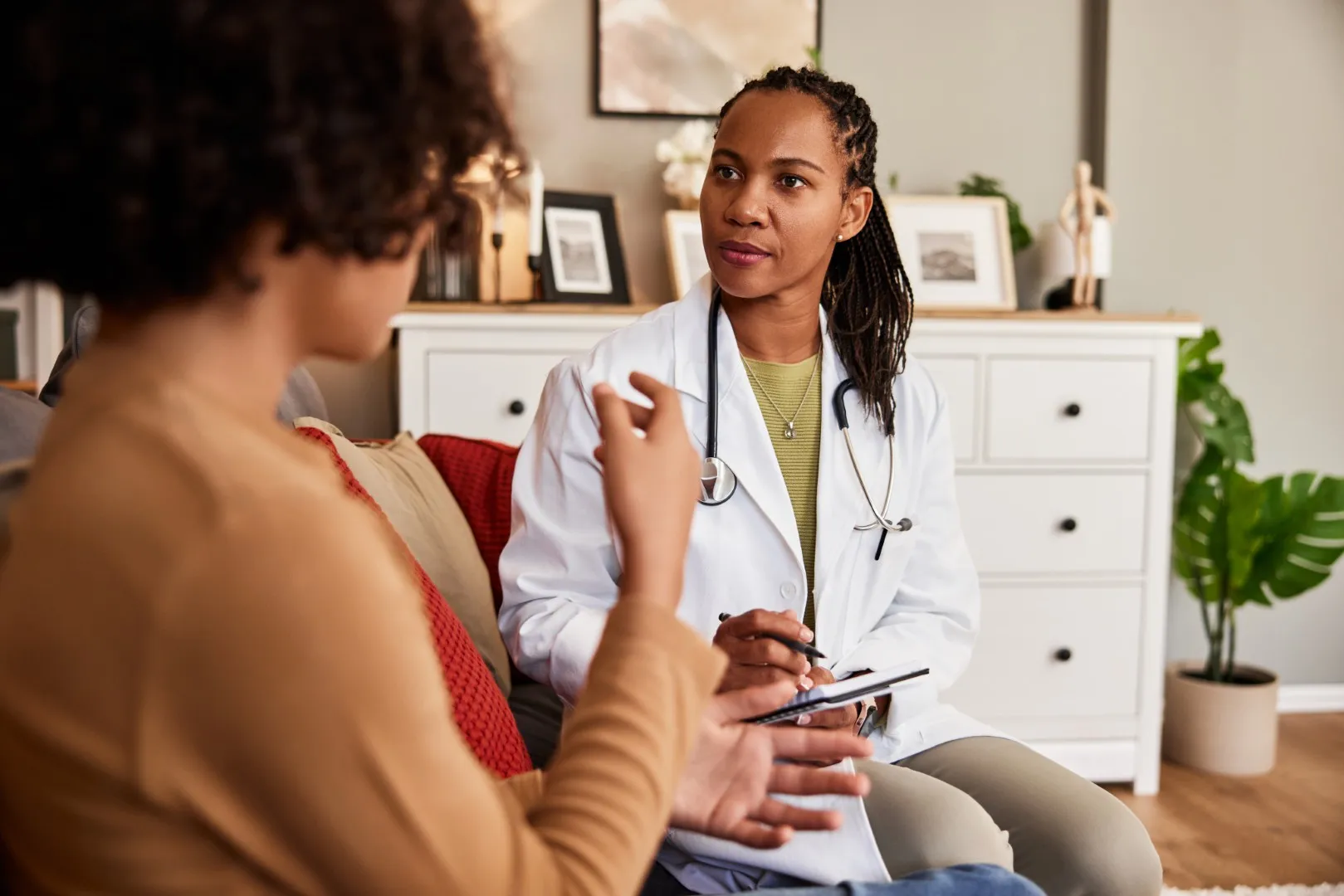 A serious African-American doctor pediatrician writing notes while talking with a boy during a home visit.